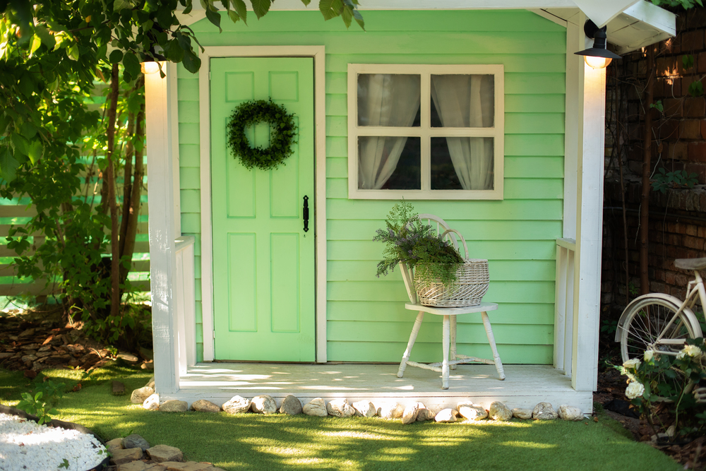 Acogedora caseta de jardín en tonos verdes y blancos, perfecta para relajarse o como espacio de almacenamiento. La decoración con plantas y detalles rústicos aporta encanto y funcionalidad al jardín, creando un rincón ideal para disfrutar de la naturaleza.